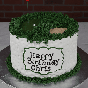The BD-117 Golf Green is a round, golf-themed birthday cake with green icing grass, a sand bunker, golf ball, red “40” flag, and “Happy Birthday Chris” written on the side.
