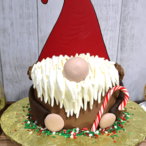 The CH-000G is a round cake decorated as a Christmas gnome, featuring a tall red hat, white frosting beard, round nose and hands, candy cane, and red, white & green sprinkles on a gold board.