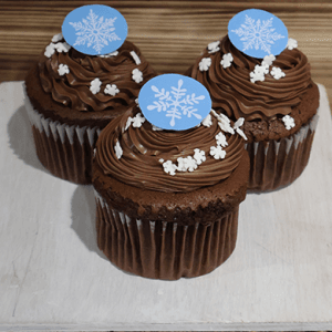 Three CH-061A Chocolate cupcakes with white filling, frosted and topped with white snowflake sprinkles and blue snowflake toppers, are displayed on a wooden board.