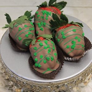 Four STP-022 Milk Chocolate dipped strawberries with green icing sit on a decorative silver cake stand with beaded trim, arranged to show their leafy tops.