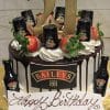 The BD-024B BaileysWithNumber is a chocolate drip cake topped with strawberries, whipped cream, mini Baileys bottles, a large gold 21 topper, and a Happy Birthday sign on the front, presented on a gold board.