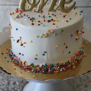 The CB-023H 6" Smash Cake features white frosting, colorful sprinkles, and a gold "one" topper, displayed on a white cake stand.