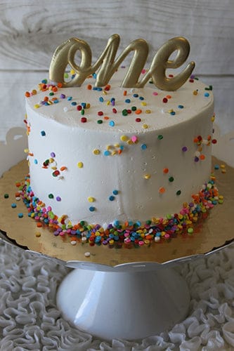 The CB-023H 6" Smash Cake features white frosting, colorful sprinkles, and a gold "one" topper, displayed on a white cake stand.