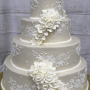 The WC-000D is a four-tiered white wedding cake featuring intricate white icing patterns and cascading white roses, elegantly displayed against a light wooden background.
