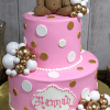 The BB-000C is a two-tiered pink cake with white and gold polka dots, topped with a fondant teddy bear in a pink bow. White and gold spheres decorate the cake, and "Hannah" is written on the lower tier.