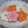The CE-040b Easter features flower-shaped cookies in pink, white, and orange with smiley faces, neatly arranged on a white scalloped plate atop decorative fabric.