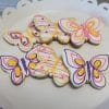 CE-040d Easter features butterfly-shaped cookies decorated with vibrant pink, yellow, and purple icing, beautifully arranged on a white scalloped cake stand.