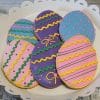 The CE-040g Easter features six egg-shaped cookies on a white plate, each decorated with pastel pink, purple, blue, and yellow icing in zigzags, dots, and bows.