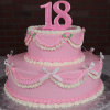 The TC-000M is a two-tiered pink and white birthday cake featuring ruffles, bows, small roses, and topped with a large pink number 18.