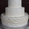 The WD-001Y is a three-tiered white cake featuring intricate scalloped icing designs, piped dots, and petal-like decorations at the base, set against a dark brick background.