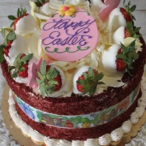 The Red Velvet Cake features red velvet layers, white frosting, strawberries, white chocolate shards, and pink bunny decorations. A pink plaque on top says "Happy Easter" in purple icing.
