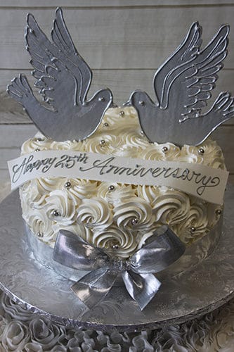 AN-022: White cake with rosette icing, silver pearls, two silver dove toppers, a silver bow, and a "Happy 25th Anniversary" banner on a silver board.