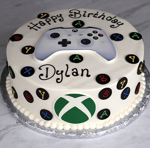 The CB-011N is a round birthday cake topped with an edible Xbox controller, colorful game controller buttons around the sides, and “Happy Birthday Dylan” written in black icing.