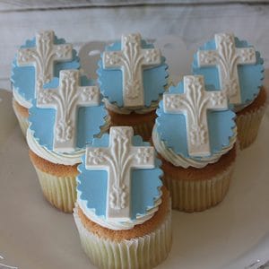 Six RC-102 Gold cupcakes with chocolate filling, topped with blue fondant circles and white crosses, are arranged on a white platter for a religious or celebratory theme.