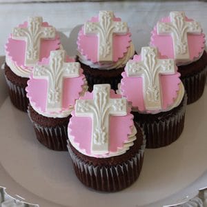 Six RC-101 Chocolate cupcakes with white chocolate mousse filling, each topped with pink fondant circles and detailed white decorative crosses, are neatly arranged on a white plate for a festive, elegant display.