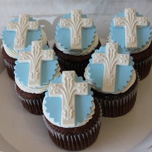 RC-103 Chocolate cupcakes with white chocolate mousse filling, decorated with white and light blue icing and a white embossed cross, are neatly arranged on a white platter.