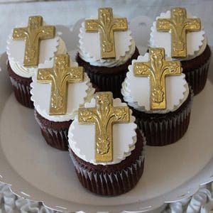Six CC-044 chocolate cupcakes with white chocolate mousse filling, topped with white icing and scalloped fondant featuring gold crosses, arranged on a white plate.