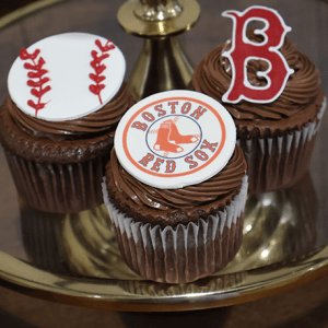 Three CC-118B chocolate cupcakes with white filling, topped with edible baseball, Boston Red Sox logo, and red "B" decorations, are displayed on a gold tray.