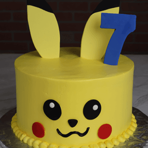 The CB-011R is a round yellow Pikachu cake featuring tall ears, black eyes, red cheeks, and a blue number 7 on top. It sits on a silver cake board with a brick background.