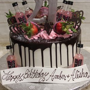 The BD-024N PinkWhitney is a white and chocolate drip cake with pink frosting, strawberries, mini Pink Whitney bottles, chocolate hearts, a silver 21 topper, and a “Happy Birthday Amber & Alisha” sign.