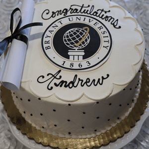 The GC-000F Bryant is a round cake featuring the Bryant University seal, "Congratulations Andrew," and a small diploma with a black ribbon, presented on a gold-edged platter.