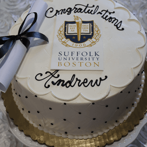 The GC-000I Suffolk University cake is white with black polka dots, gold trim, the Suffolk University Boston logo, "Congratulations Andrew," and a diploma tied with a black ribbon on top.