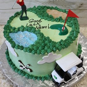 ST-007C Golf Scene: Round golf-themed cake with green frosting, golfer figurine, red flag, sand trap, water feature, "Good Luck Neve!" in icing, and a small toy golf cart at the base.
