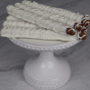 Four DB-000I White Dipped Pretzel rods, coated in white chocolate and topped with white sprinkles and drizzle, are displayed on a textured white cake stand against a marble background.