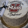 GC-000L UMass round cake with a UMass logo, "Congratulations Andrew" in black icing, white frosting with black dots, a rolled diploma tied with a black ribbon on top, presented on a gold-edged tray.