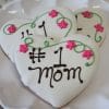 CE-050c Mother's Day: Heart-shaped cookies with white icing, pink flowers, and green vines on a white plate, each inscribed with “#1 mom” in brown icing.