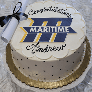 The GC-000Q Mass Martime is a round white cake featuring “MARITIME” on a blue and yellow logo, topped with “Congratulations Andrew” in black icing and a rolled diploma with a black ribbon.