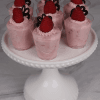 Seven CO-106 Raspberry Shooters—small clear cups of pink mousse topped with a raspberry and chocolate decor—are arranged on a white cake stand against a marble background.