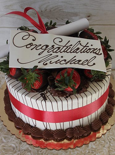 GC-002A is a decorated cake with white icing, chocolate stripes, chocolate-dipped strawberries, a red ribbon, and a “Congratulations Michael” card in cursive. A rolled-up parchment sits on top.