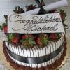 GC-003 is a round cake adorned with chocolate-dipped strawberries, chocolate drizzle, a black ribbon, and a scroll. A white plaque on top displays “Congratulations Michael” in elegant script.