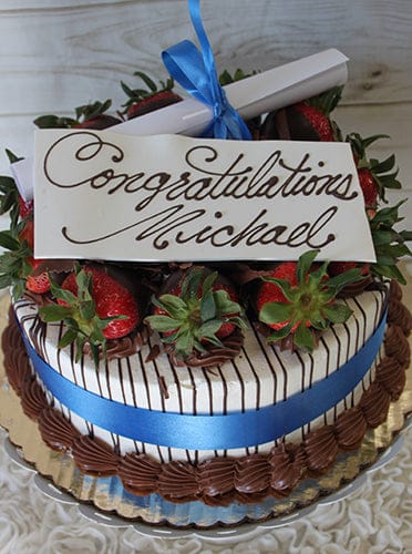 GC-005 is a decorated cake featuring chocolate-covered strawberries, a blue ribbon, and a white chocolate plaque reading "Congratulations Michael" in cursive, topped with a rolled-up paper tied with a blue ribbon.