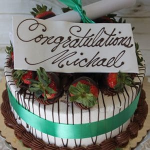 GC-006: A decorated cake topped with chocolate-dipped strawberries, a green ribbon, and a white card reading "Congratulations Michael" in cursive. Includes a rolled paper scroll tied with a green ribbon on top.