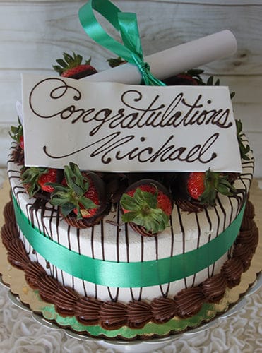 GC-006: A decorated cake topped with chocolate-dipped strawberries, a green ribbon, and a white card reading "Congratulations Michael" in cursive. Includes a rolled paper scroll tied with a green ribbon on top.