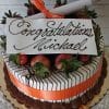 The GC-007 is a decorated cake with chocolate drizzles, strawberries, an orange ribbon, and a diploma topper. A white plaque reads "Congratulations Michael" in elegant script.