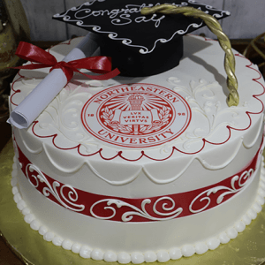 The GC-042B Northeastern is a round graduation cake with white icing, a red Northeastern University seal, red and white ribbon, fondant diploma, black graduation cap with gold tassel, and “Congrats” on top.