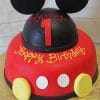 CB-002F is a two-tiered birthday cake decorated like Mickey Mouse, featuring black fondant ears, yellow buttons, "Happy Birthday" on the red lower tier, and "Xavier 1" in red and yellow icing on the top tier.