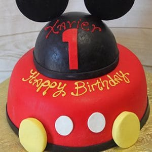 CB-002F is a two-tiered birthday cake decorated like Mickey Mouse, featuring black fondant ears, yellow buttons, "Happy Birthday" on the red lower tier, and "Xavier 1" in red and yellow icing on the top tier.