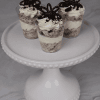 Three CO-105 Oreo Shooters, featuring layers of cream and cookie crumbles, topped with whipped cream, chocolate accents, and cookie crumbs, are displayed on a beaded-edge white cake stand.