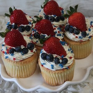 JC-024 Gold cupcakes filled with chocolate mousse, topped with swirls of frosting, and decorated with fresh strawberries, blueberries, and gold star-shaped sprinkles on a white plate.