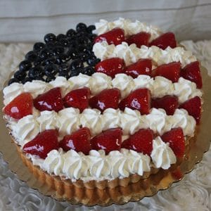 The JC-014 is a round tart decorated as an American flag with blueberries for the blue field, strawberries for the red stripes, and whipped cream for the white stripes, displayed on a gold tray.