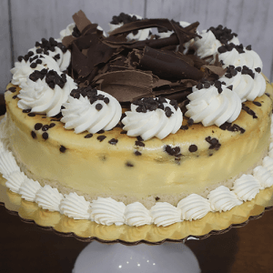 GD-013 Chocolate Chip Cheesecake, topped with swirls of whipped cream, chocolate shavings, and chocolate chips, is displayed on a cake stand with piped whipped cream around the base.