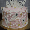 HW-000B is a pink frosted cake topped with white chocolate ghosts, white icing lines, yellow star decorations, and presented on a gold cake board.