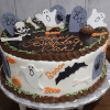 The HW-001 is a round Halloween-themed birthday cake featuring ghosts, tombstones, bats, bones, pumpkins, spiders, and "Happy Birthday Nick" written in orange icing.