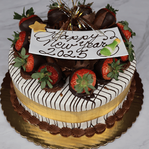 The NY-001 Strawberry Grand Marnier is a round cake topped with chocolate-dipped strawberries, chocolate drizzle, a gold ribbon, and a “Happy New Year 2025” sign. It sits on a gold board with a marble background.