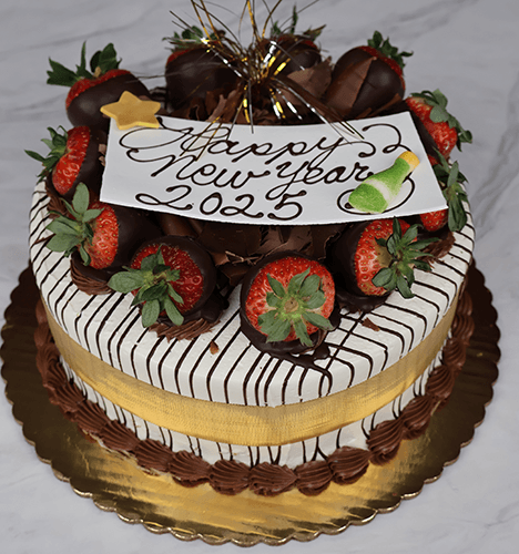 The NY-001 Strawberry Grand Marnier is a round cake topped with chocolate-dipped strawberries, chocolate drizzle, a gold ribbon, and a “Happy New Year 2025” sign. It sits on a gold board with a marble background.