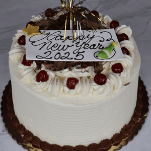 The NY-004 Black Forest cake is a round white frosted treat adorned with whipped cream swirls, cherries, chocolate pieces, and a gold topper. A card atop the cake says “Happy New Year 2025” in chocolate icing.